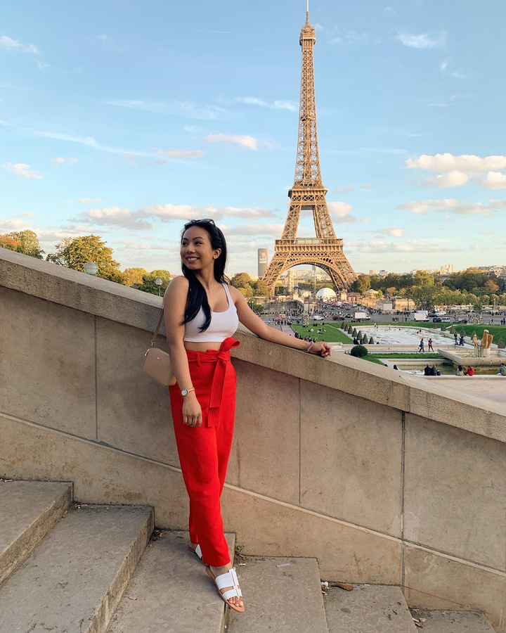 a young woman in red pants standing in front of the Eiffel Tower on a sunny day looking away and smiling. she is wearing Aritzia pants and a Melie Bianco shoulder purse.